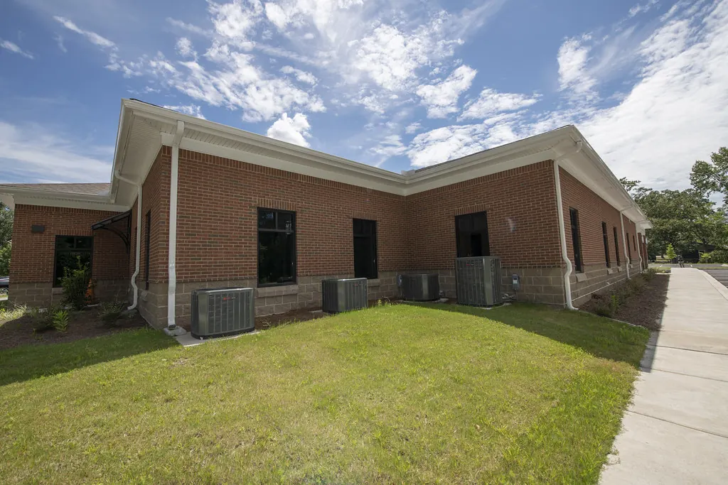 Row of AC condensers beside a brick building and lawn