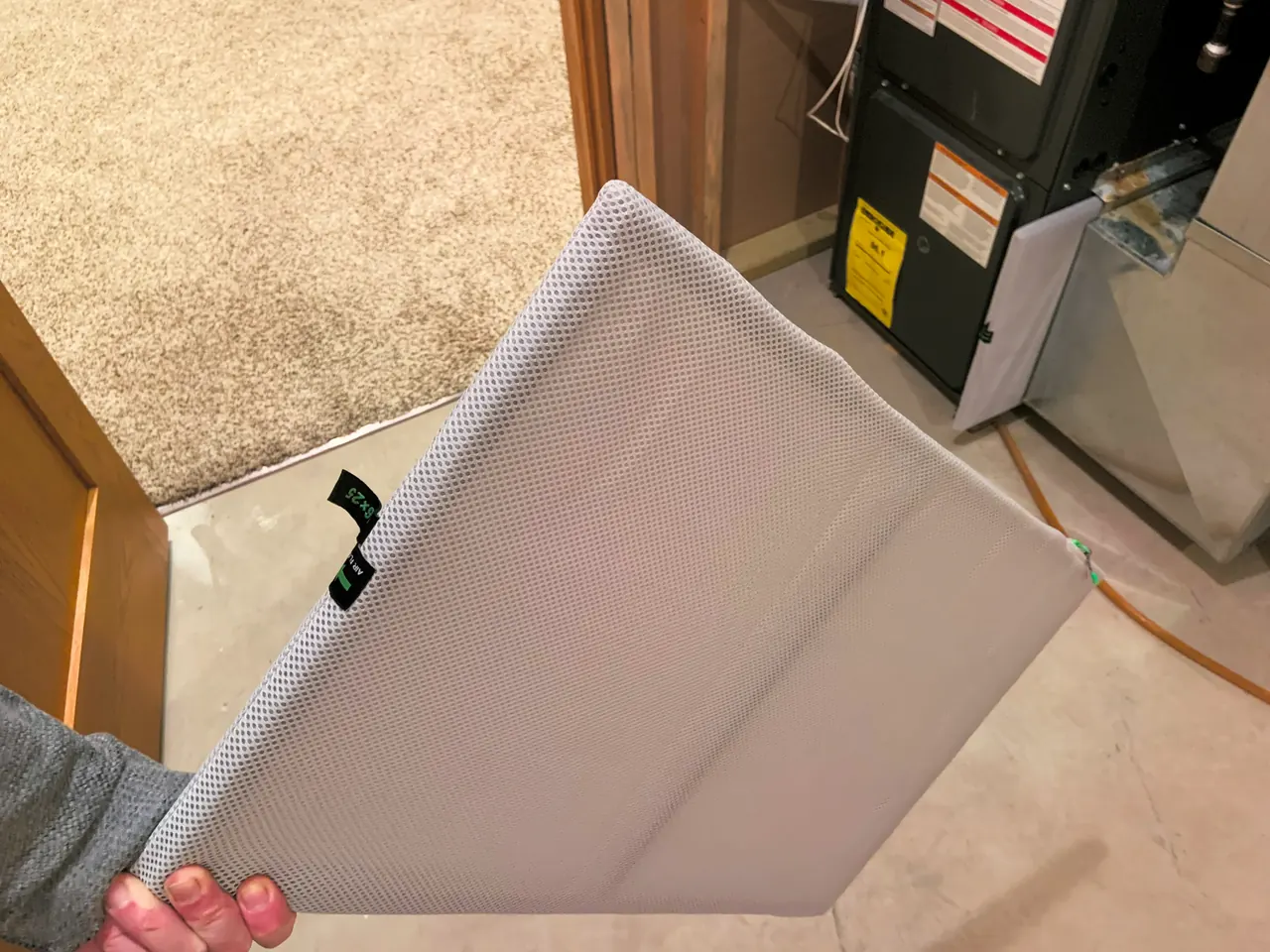 Hand holding a pleated air filter in front of an open home furnace